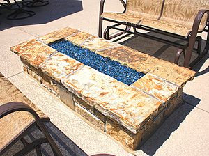 Concrete patio with rectangular gas burning fire pit with stone masonry and flagstone cap