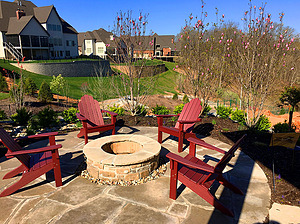 Flagstone patio with red chairs and round wood burning fire pit with stone masonry and flagstone cap