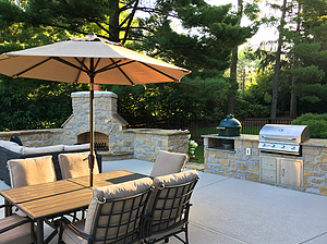Concrete patio with stone fireplace, outdoor kitchen and beige furniture