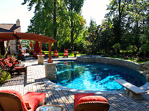 st. louis custom designed freeform concrete pool, wood pergola, brick paver patio, jump board, red outdoor furniture, raised wall
