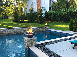 St. Louis custom designed geometric concrete pool with raised wall with stone veneer and stone columns with fire water bowls