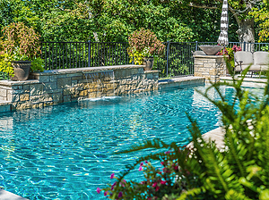 St. Louis custom designed geometric concrete pool with flagstone coping, raised wall with stone veneer, sheer descent and stone columns with fire bowls and planters