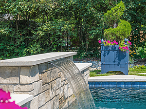 Manicured topiary next to St. Louis custom designed geometric concrete pool with raised wall with stone veneer and sheer descent water feature