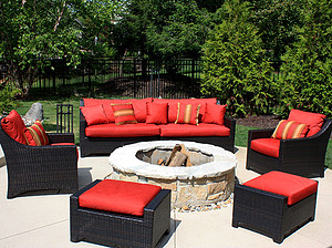 Concrete patio with black and red furniture and round wood burning fire pit with stone masonry and flagstone cap