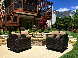 Concrete patio with brown and beige patio furniture and round, gas burning fire pit with stone masonry 