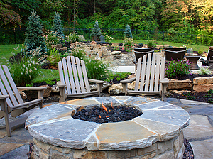 Flagstone patio with beige chairs and round gas burning fire pit with stone masonry and flagstone cap