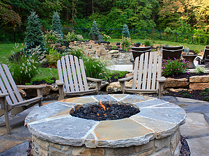 Flagstone patio with beige chairs and round gas burning fire pit with stone masonry and flagstone cap