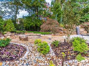 Landscaped flagstone patio with round wood burning fire pit with stone masonry, flagstone cap and boulder seating
