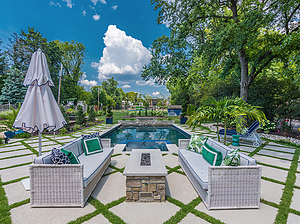 Segmented concrete patio with white wicker furniture and rectangular gas fire pit with stone veneer and pewter mist cut stone cap