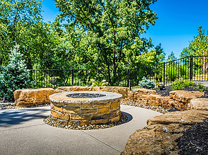 Concrete patio with round gas fire pit with stone masonry, flagstone cap and boulder seating wall