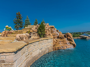 St. Louis custom designed concrete pool with raised wall with stone veneer and ledgerock steps leading to slide atop large boulder water feature