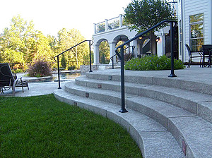 Textured concrete steps with black hand rail leading up to patio