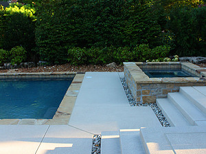 Textured concrete steps leading from pool area to concrete spa with flagstone coping and exposed walls with stone veneer