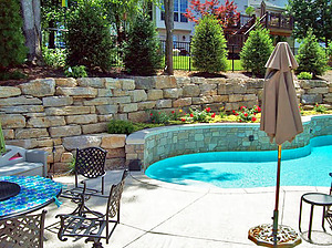 Landscaped boulder retaining wall next to freeform St. Louis custom designed concrete pool with raised wall with stone veneer