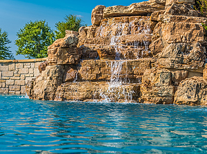 St. Louis custom designed concrete pool with raised wall with stone veneer and large boulder water feature