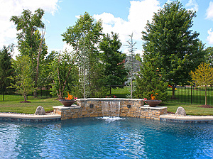 St. Louis custom designed freeform concrete pool with raised wall with stone veneer, two medallions, two fire bowls and sheer descent