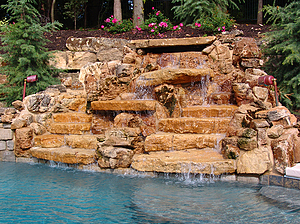 St. Louis custom designed concrete pool with large boulder water feature with pink flowers and landscape lighting