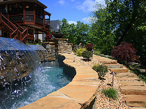 Ledge rock steps leading up to St. Louis custom designed freeform concrete pool with flagstone coping and tiled vanishing edge