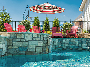 Red chairs overlooking St. Louis custom designed freeform concrete pool with raised wall with stone veneer and raised concrete spa with spillway water feature