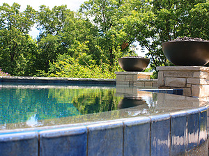 St. Louis custom designed freeform concrete pool with stone columns with fire bowls and vanishing edge water feature with blue tile