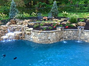 Landscaped St. Louis custom designed freeform concrete pool with raised wall with stone veneer, flagstone coping, boulder water feature and stone columns with scuppers