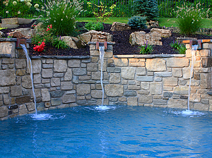 Landscaped St. Louis custom designed freeform concrete pool with raised wall with stone veneer and stone columns with copper scuppers