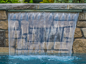 St. Louis custom designed concrete pool with raised wall with stone veneer, flagstone coping and sheer descent water feature