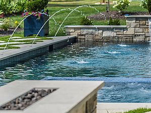 Fire pit next to St. Louis custom designed geometric concrete pool with cut stone coping, water crystal jets, and raised wall with stone veneer and sheer descent