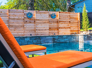 St. Louis custom designed concrete pool with raised stone wall, sheer descent, wooden privacy fence and yellow lounge chairs