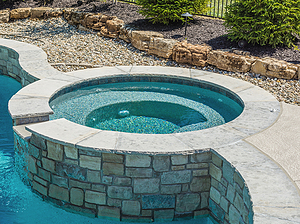 st. louis custom designed freeform concrete pool, raised concrete spa with stone veneer, flagstone cap and spillover feature